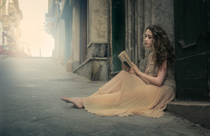 Young woman in flowing dress sitting on a step reading a book